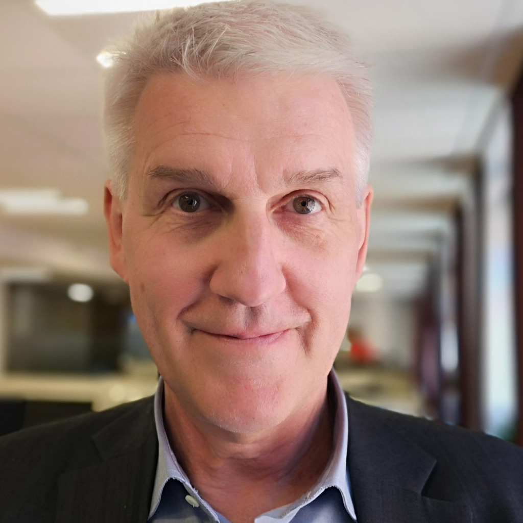 Claes Lindgren, En medelålders man med kort grått hår, klädd i mörk kostymjacka och ljusblå skjorta, står inomhus mot en kontorskuliss, som påminner om en scen från Anna Kinberg Batras rapport om arbetsmiljökartläggning. Han stirrar direkt mot kameran med ett neutralt uttryck.