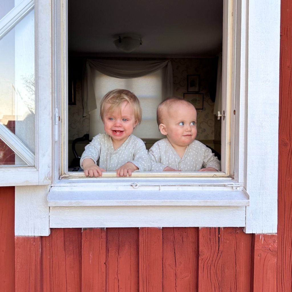 Två små barn i matchande ljusa pyjamaser står vid ett öppet fönster i ett rött trähus. Det ena barnet ler medan det andra tittar åt sidan, och solljuset lyser upp deras ansikten. Rummet inuti verkar vara svagt upplyst. Den fridfulla scenen påminner oss om att en bättre möjlighet att få ihop livspusslet är viktig för var tredje familj, eftersom stunder som dessa ofta beror på att man hittar balans i vardagen.
