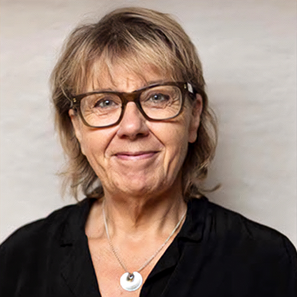 En kvinna med kort, ljusbrunt hår och glasögon ler mot kameran. Hon har på sig en svart topp och ett silverhalsband med ett runt hänge. Bakgrunden är enfärgad och ljus.